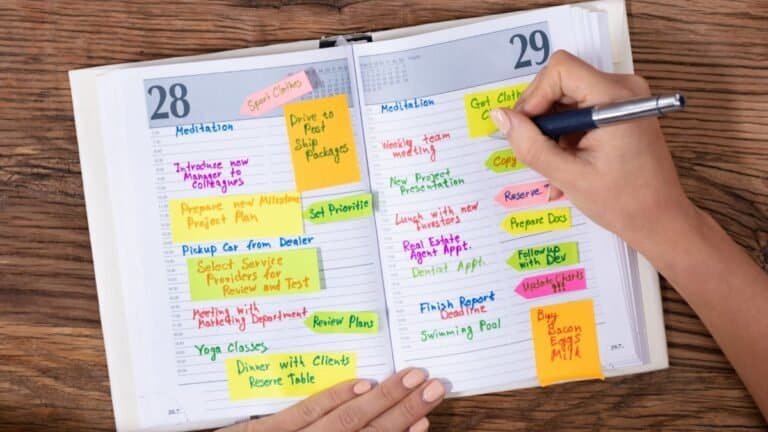 Hand writing in colorful planner with time blocks and sticky notes