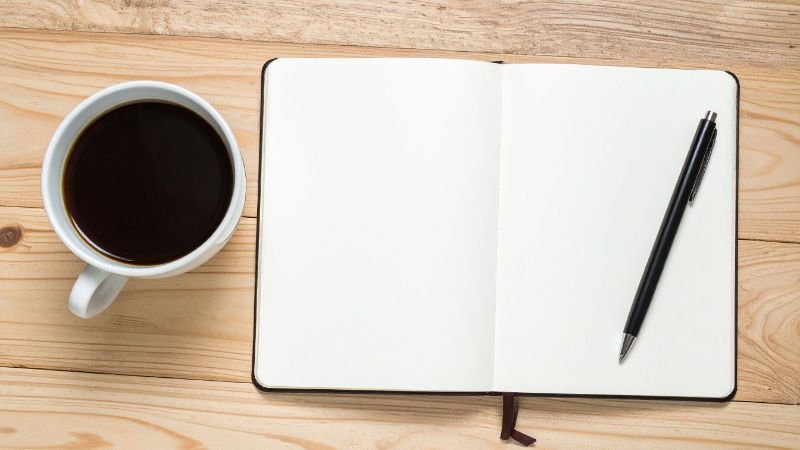 A coffee cup next to a journal on a wooden desk, representing different habit triggers in a morning routine