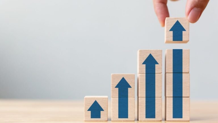 Hand stacking wooden blocks with upward arrows showing habit stacking progression