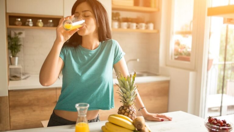 Woman drinking fresh orange juice in bright kitchen showing healthy morning routine habits